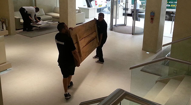 Two gladiator removal men carrying a crate through a lobby,
